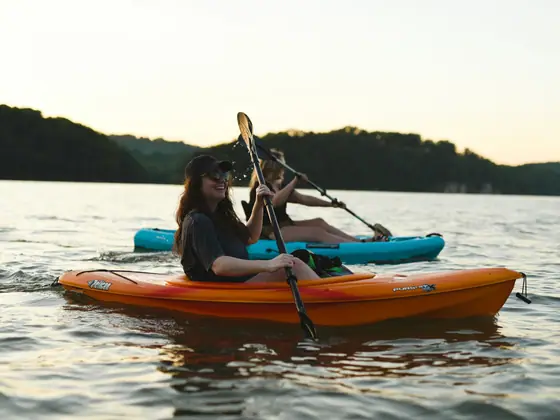 Deux femmes dans un kayak orange à la lumière dorée de fin de journée, devant une ligne d'arbres