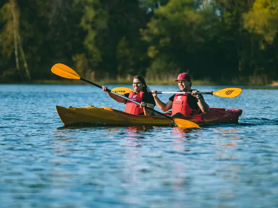 Deux kayakistes en gilet rouge pagaient côte à côte dans un kayak jaune sur un lac calme