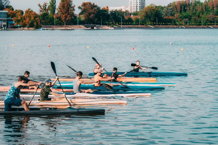 Une équipe de pagayeurs alignés sur l'eau, pagaies levées, au départ d'une régate