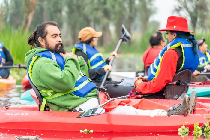 Un groupe en gilets bleus installé dans des kayaks rouges sur une eau calme, entre des roseaux