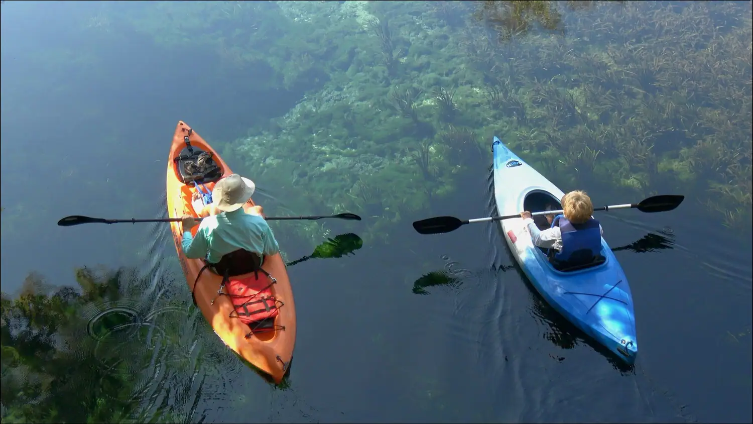 Deux kayaks, un orange et un bleu, vus du ciel sur une eau sombre et verte