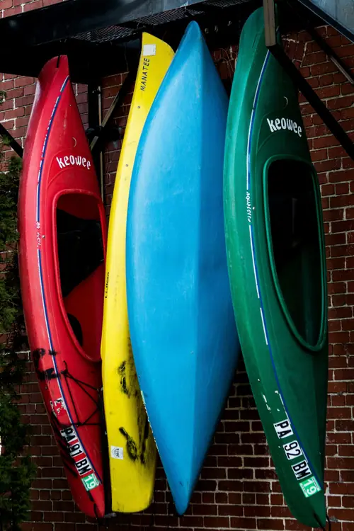 Des kayaks rouge, jaune, bleu et vert dressés côte à côte contre un mur de briques