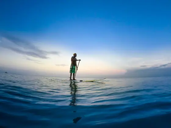 Une silhouette debout sur un paddle, au loin, sur une eau bleue sous un ciel dégagé